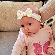 Amélia a rejoint le concours — aidez-le/la à gagner de superbes lots ! adult_hand, baby, bow, butterfly_print, child, couch, cozy, curious_expression, cushion, cute, hand, headband, indoors, infant, person, pink_clothing, portrait, seated, skin, soft_fabric