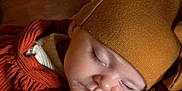 Athena is registered to the contest to win money with this photo: baby, sleeping, hat, brown, orange, clothing, hand, face, peaceful, infant, portrait, closeup, wood, texture, soft_light, warm_colors, resting, cute, child, cozy