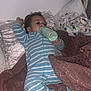 baby, bottle, bed, blanket, pillow, child, sleepwear, striped_clothing, infant, lying_down, indoors, cozy, feeding, soft_texture, resting, person, cute, relaxed, home, sleep