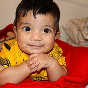 Izhak participe au concours pour gagner de l'argent avec cette photo : baby, child, closeup, clothing, cute, expression, eyes, face, hair, hands, happy, indoors, infant, lying_down, person, portrait, red_blanket, skin, smile, yellow_shirt