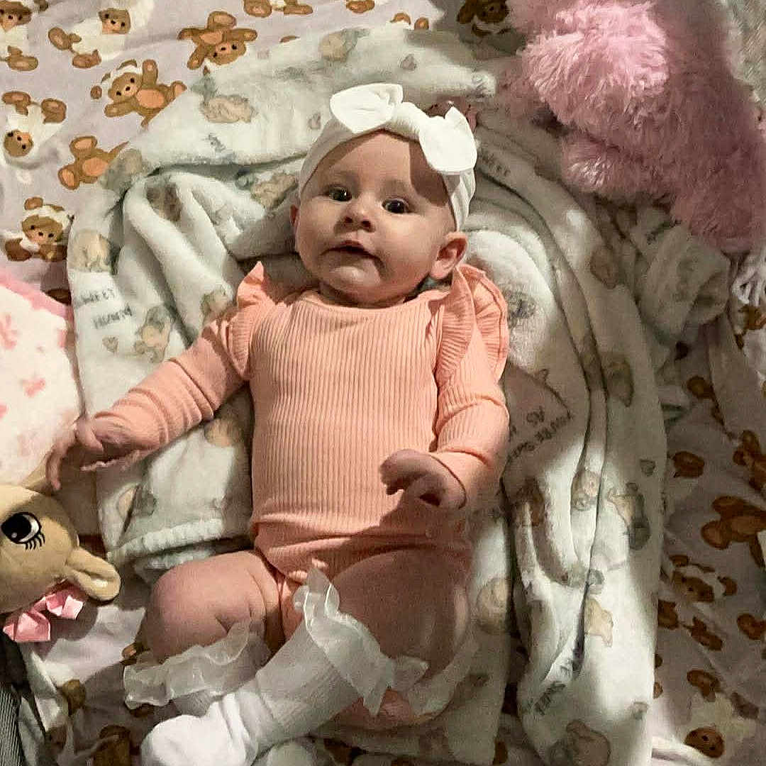 Sarah joined the competition — help win amazing prizes! baby, blanket, bow, child, comfortable, cozy, cute, headwear, indoors, infant, lying_down, nursery, pink_clothing, plush_toy, portrait, smiling, socks, soft_toys, teddy_bear_pattern, young_child