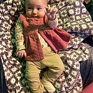 Madeline joined the competition — help win amazing prizes! baby, infant, blanket, patterned_blanket, pink_vest, beige_pants, socks, lying_down, indoor, cute, young_child, soft_texture, cozy, warm_clothing, small_hands, face, curious, comfort, resting, furniture