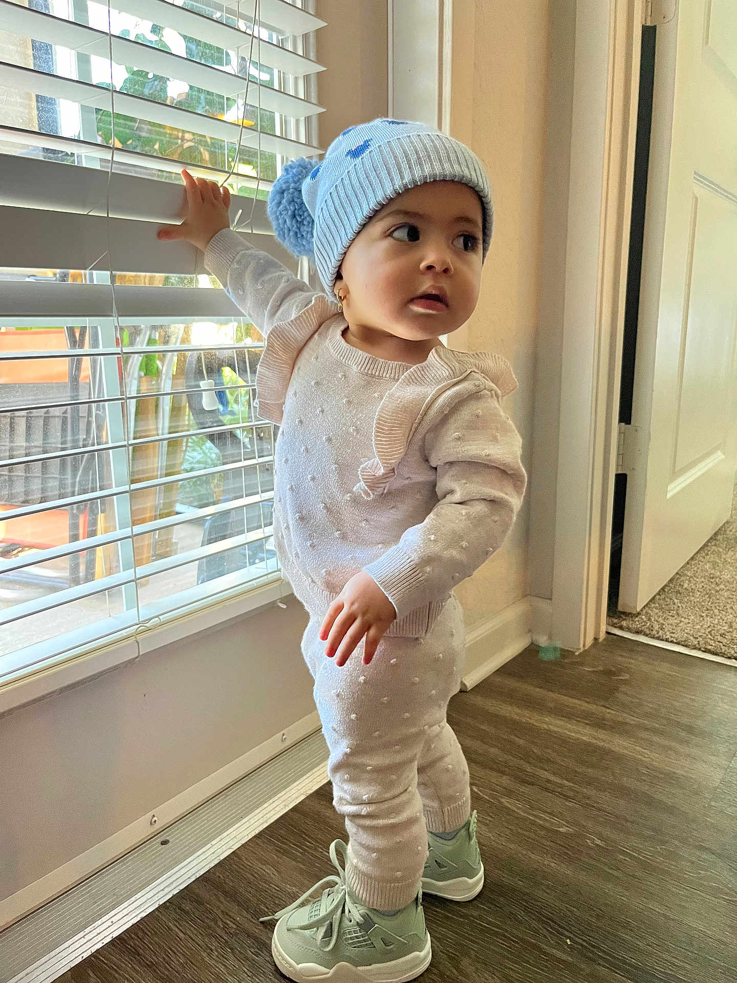 Fernanda joined the competition — help win amazing prizes! toddler, child, window, blinds, hat, pom_pom, knitwear, sneakers, floor, indoor, curious, exploration, standing, light, door, carpet, hand, face, expression, clothing