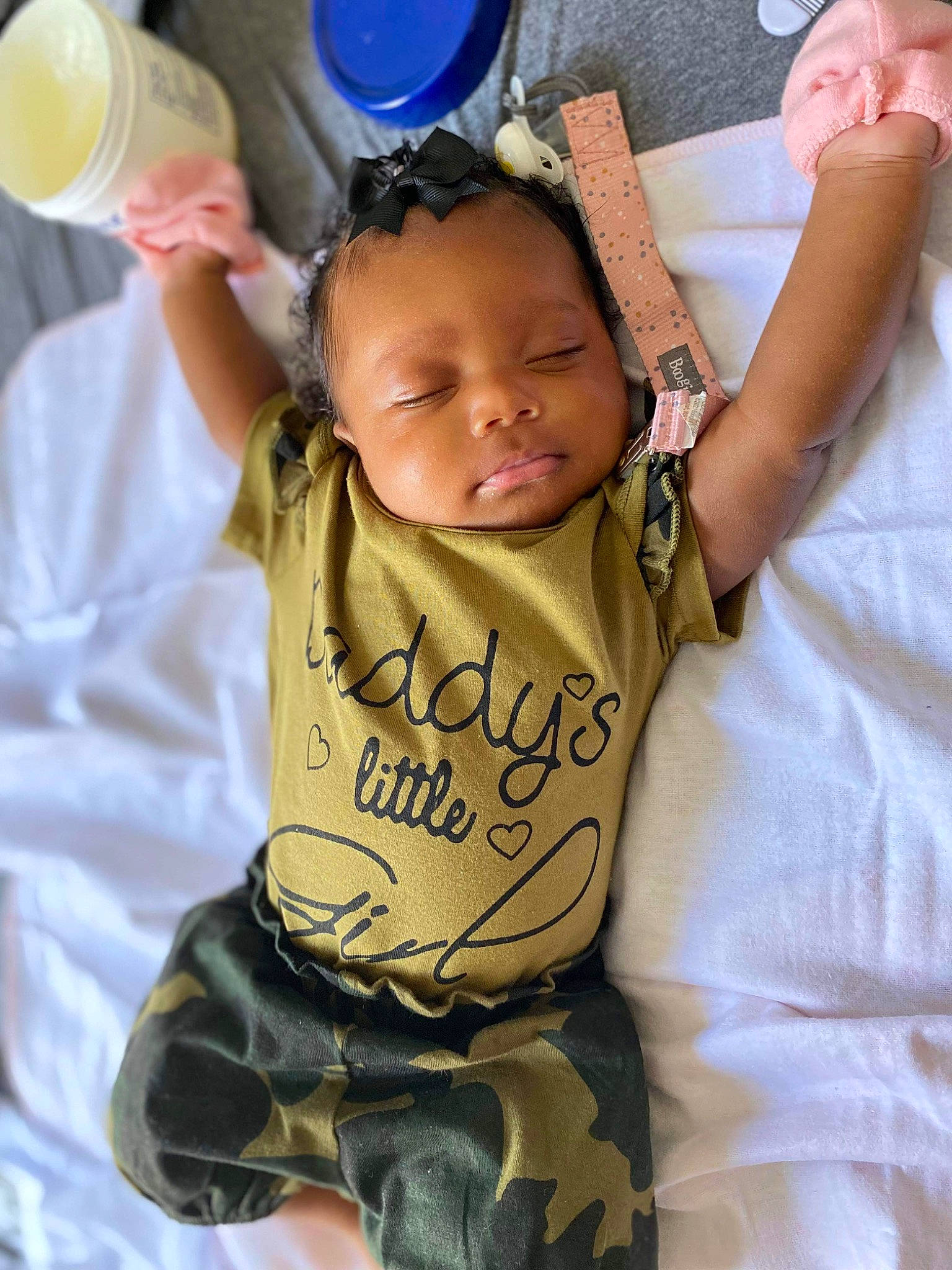 Aubree is registered to the contest to win money with this photo: arm, baby, baby_toddler_clothing, blue, child, cool, finger, fun, gesture, hand, happy, military_camouflage, person, product, sitting, skin, sleeve, t_shirt, thumb, toddler