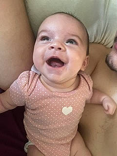 Isla is registered to the contest to win money with this photo: baby, cheek, chin, eye, eyebrow, finger, gesture, happy, head, human_body, iris, lip, mouth, neck, nose, person, pink, skin, sleeve, smile