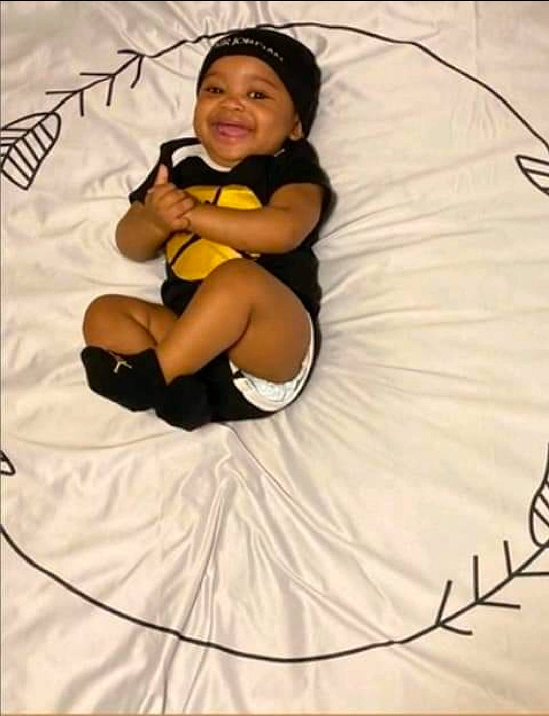 Da' Mori is registered to the contest to win money with this photo: arm, baby, child, comfort, elbow, event, fashion_accessory, flash_photography, flooring, foot, fun, happy, headwear, human_leg, joy, knee, person, recreation, sitting, smile