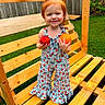 toddler, child, red_hair, apple, orange, wooden_swing, garden, grass, fence, playful, smiling, outdoor, summer, fruit_pattern, clothing, happy, cute, nature, daylight, standing