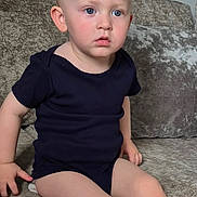 Carson is registered to the contest to win money with this photo: toddler, child, baby, sitting, couch, indoor, blue_eyes, onesie, furniture, blond_hair, expression, person, home, portrait, young_child, casual_clothing, curious, seat, living_room, skin
