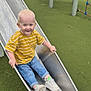 Carson joined the competition — help win amazing prizes! child, toddler, slide, playground, yellow_shirt, striped_shirt, blue_jeans, white_sneakers, metal_slide, grass, outdoor, smile, happy, fun, play, person, casual_clothing, daylight, young_child, active
