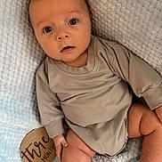 Lakelyn joined the competition — help win amazing prizes! baby, infant, three_months, milestone, blanket, beige_clothing, sitting, cute, wide_eyes, portrait, soft_texture, wooden_sign, indoor, child, young, skin, expression, hand, foot, closeup