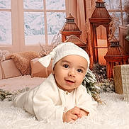 Eyden a rejoint le concours — aidez-le/la à gagner de superbes lots ! baby, infant, white_clothing, hat, smiling, lying_down, fluffy_rug, lanterns, decorations, winter, snow, window, curtains, gift_box, cozy, indoors, holiday, festive, cute, portrait