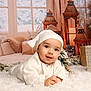 baby, infant, white_clothing, hat, smiling, lying_down, fluffy_rug, lanterns, decorations, winter, snow, window, curtains, gift_box, cozy, indoors, holiday, festive, cute, portrait