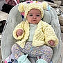 baby, infant, knit_hat, knit_cardigan, baby_seat, floral_pattern, blue_eyes, socks, leggings, indoor, cushion, furniture, living_room, table, blanket, person, child, cute, seated, warm_clothing