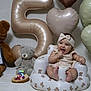 baby, infant, teddy_bear, balloon, number_5, cake, headband, smile, celebration, inflatable_chair, heart_shaped_balloon, person, cute, child, soft_lighting, white_background, happy, sitting, plush_toy, birthday