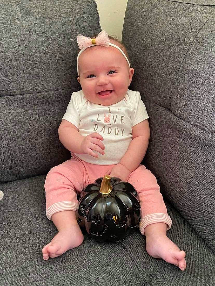 Roselina is registered to the contest to win money with this photo: baby, baby_toddler_clothing, cheek, comfort, couch, eye, face, flash_photography, floor, flooring, foot, happy, head, human_leg, joy, knee, person, sitting, sleeve, smile