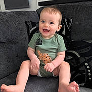 Freddie is registered to the contest to win money with this photo: baby, child, smiling, sitting, couch, green_onesie, happy, indoor, infant, playful, cute, portrait, furniture, living_room, person, small_child, feet, hands, face, expression