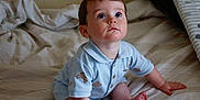 Freddie is registered to the contest to win money with this photo: baby, bed, bedding, blue_clothing, child, curious, cute, expression, face, foot, hand, indoors, infant, looking_up, person, portrait, romper, sitting, skin, young