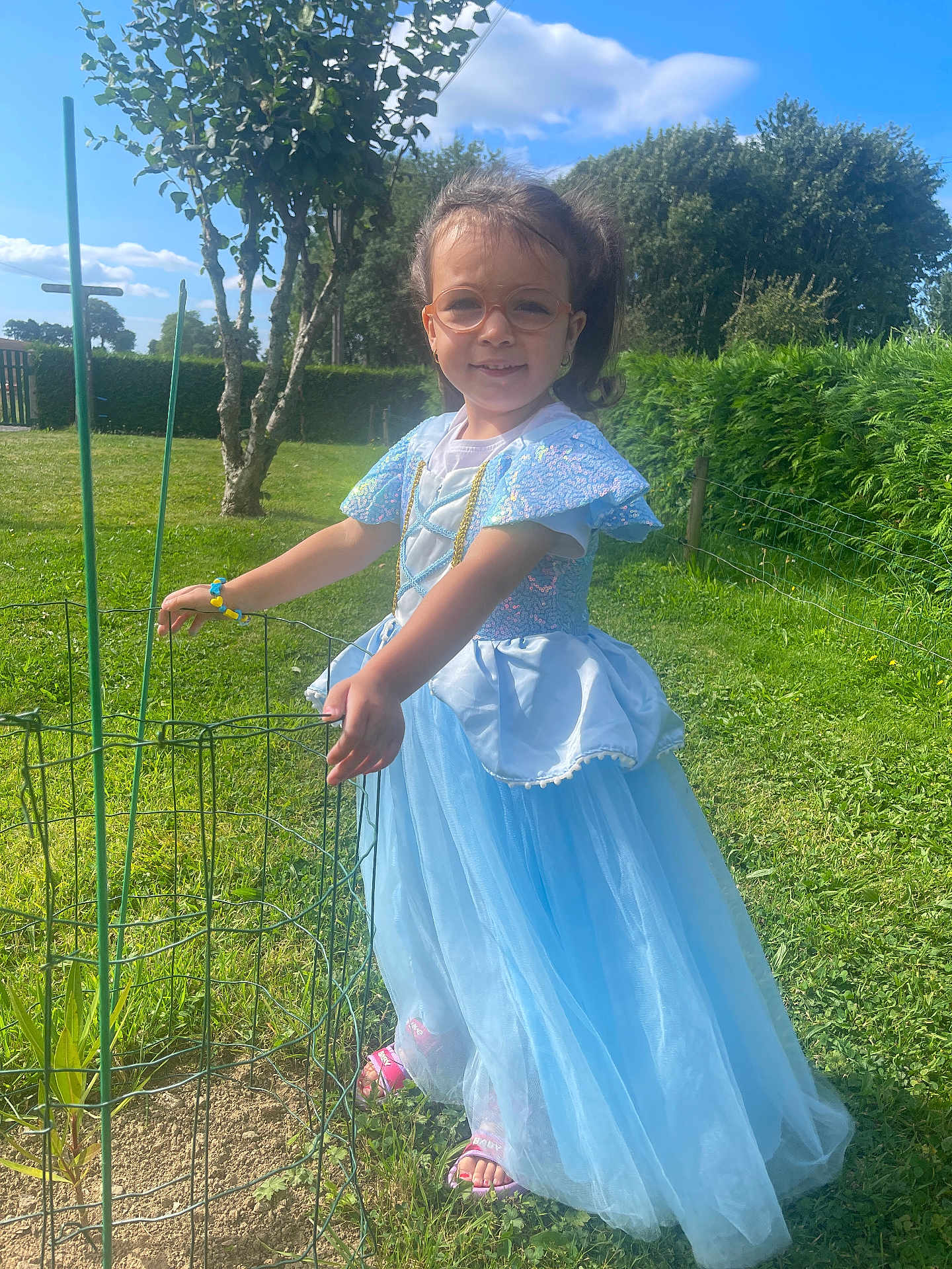 Séréna a rejoint le concours — aidez-le/la à gagner de superbes lots ! child, girl, princess_dress, blue_dress, glasses, outdoor, grass, tree, plant_protection, sunny, smile, bracelet, sandals, greenery, nature, fence, happy, daylight, portrait, fashion