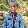 child, smiling, denim_jacket, outdoor, nature, waterfall, rocks, stream, greenery, trees, people, happy, portrait, casual_clothing, adventure, daylight, exploring, forest, young_girl, travel