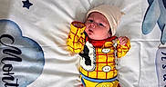 Milan is registered to the contest to win money with this photo: baby, infant, child, toy_story, woody_costume, costume, hat, red_socks, yellow_outfit, blanket, clouds, stars, lying_down, portrait, face, eyes_open, indoors, nursery, colorful, cute