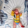 baby, infant, child, toy_story, woody_costume, costume, hat, red_socks, yellow_outfit, blanket, clouds, stars, lying_down, portrait, face, eyes_open, indoors, nursery, colorful, cute