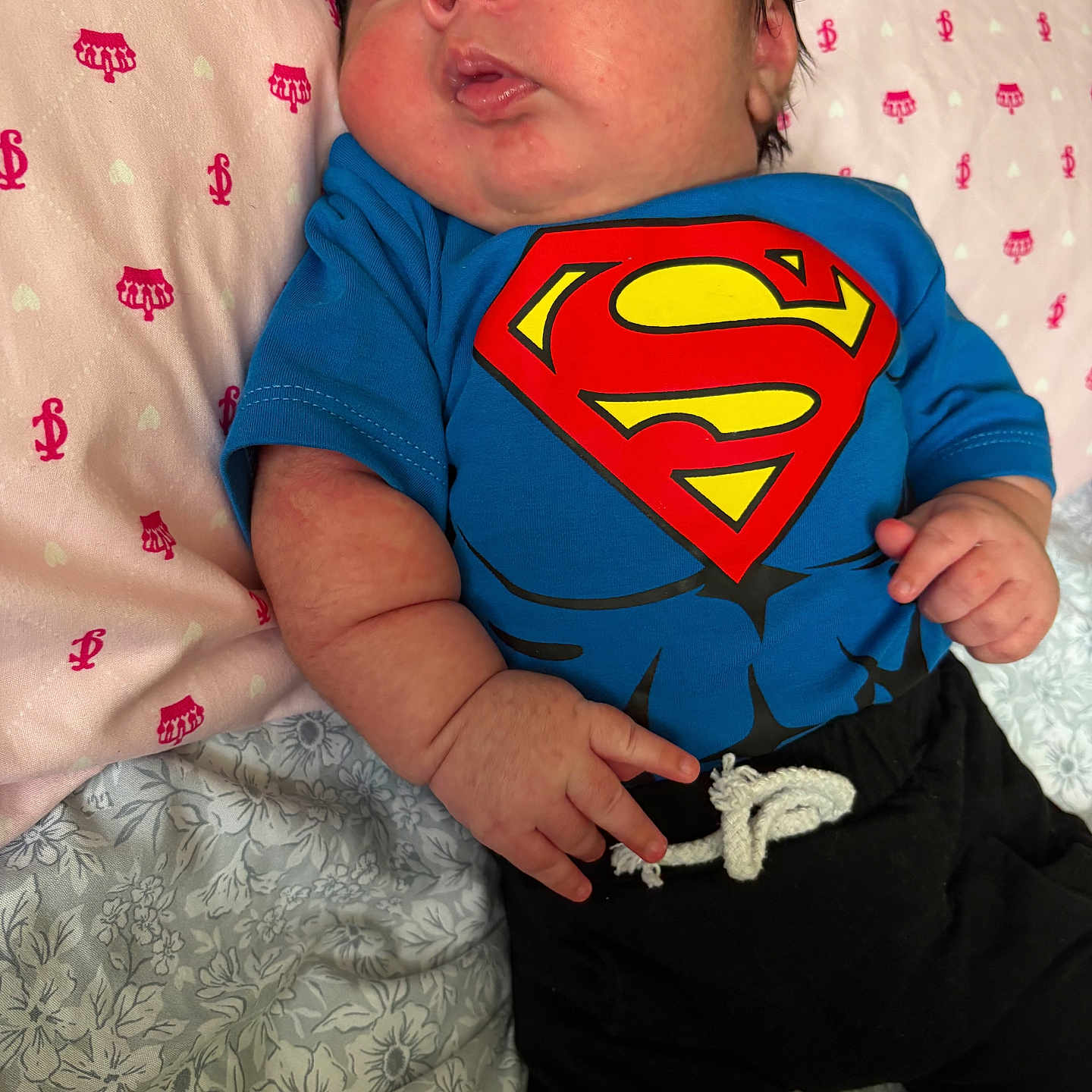 Milan joined the competition — help win amazing prizes! newborn, baby, infant, child, superman, superhero, blue_shirt, black_pants, lying_down, portrait, face, eyes, hands, bed, blanket, bedding, indoors, patterned_fabric, serious_expression, close_up