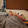 baby, child, smiling, bedroom, bed, blanket, bedding, pajamas, pink_clothing, toy, stuffed_animal, nursery, indoor, portrait, happy, lying_down, cozy, window_blinds, bedside_table, household_items