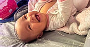 Avyanna is registered to the contest to win money with this photo: baby, infant, sleeping, yawning, lying_down, portrait, face, indoors, bed, blanket, pink_clothing, white_clothing, soft_lighting, cozy, nursery, textile, plush_blanket, patterned_bedding, home, close_up