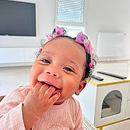 Tyah a rejoint le concours — aidez-le/la à gagner de superbes lots ! toddler, child, baby, smiling, happy, curly_hair, bows, pink_sweater, indoor, modern_room, table, furniture, face, person, cute, playful, closeup, hand, fingers, joy