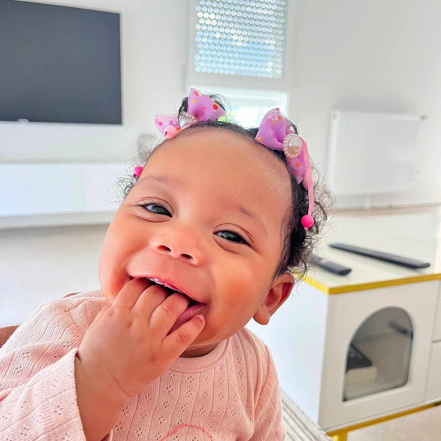 Tyah a rejoint le concours — aidez-le/la à gagner de superbes lots ! baby, bows, child, closeup, curly_hair, cute, face, fingers, furniture, hand, happy, indoor, joy, modern_room, person, pink_sweater, playful, smiling, table, toddler