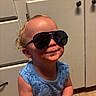 Atlas is registered to the contest to win money with this photo: child, toddler, baby, portrait, sunglasses, smiling, funny, indoor, kitchen, cabinets, floor, blue_shirt, sleeveless, blond_hair, curly_hair, face, person, standing, playful, casual