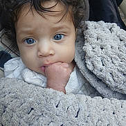 Nylah is registered to the contest to win money with this photo: baby, blue_eyes, blanket, child, closeup, curly_hair, face, fist, hand, infant, indoors, person, portrait, skin, soft_texture, warm, wrapped, cute, young_child, cozy