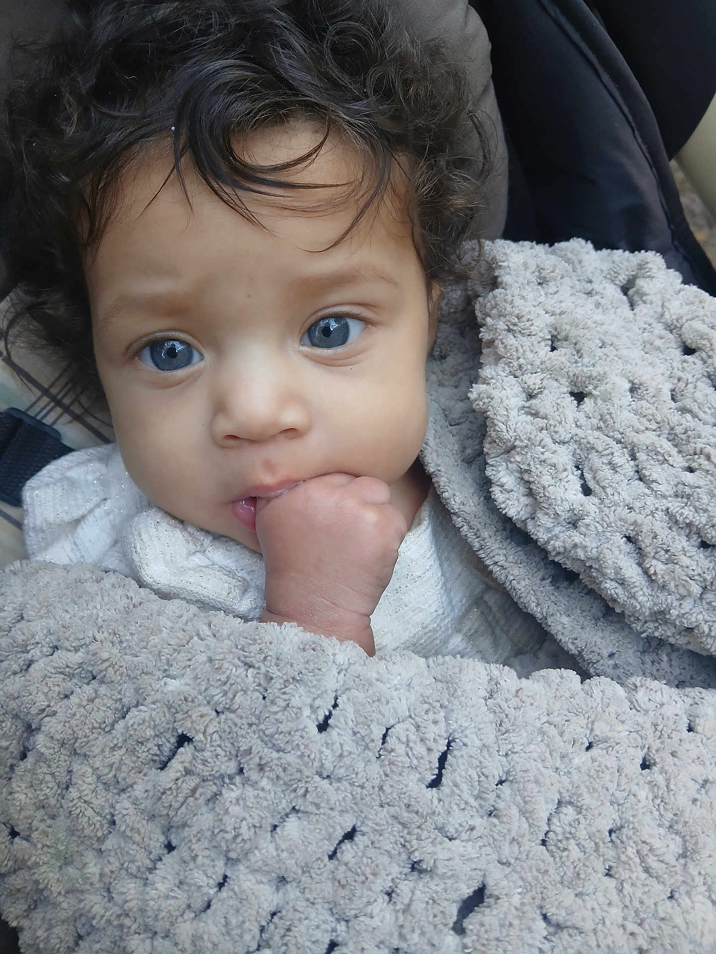 Nylah is registered to the contest to win money with this photo: baby, blue_eyes, blanket, child, closeup, curly_hair, face, fist, hand, infant, indoors, person, portrait, skin, soft_texture, warm, wrapped, cute, young_child, cozy