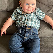 Waylon joined the competition — help win amazing prizes! baby, child, couch, plaid_shirt, blue_jeans, socks, smile, indoor, face, person, seated, furniture, cute, young_child, relaxed, casual_clothing, blue_eyes, bald, happy, infant