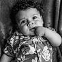 baby, child, face, curly_hair, hand, finger, shirt, patterned_clothing, black_and_white, portrait, lying_down, blanket, texture, closeup, expression, cute, infant, person, soft, indoor