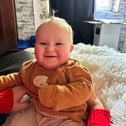 Kayden participe au concours pour gagner de l'argent avec cette photo : baby, child, smile, happy, rosy_cheeks, blond_hair, brown_clothing, blanket, indoor, person, couch, hand, red_sleeve, window, curtain, soft_texture, face, infant, cozy, portrait