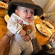 Amara joined the competition — help win amazing prizes! baby, hat, smile, polka_dot, bear, clothing, tattoo, hand, table, glass, plate, food, dining, happy, person, indoor, cute, infant, sitting, family