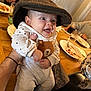 baby, hat, smile, polka_dot, bear, clothing, tattoo, hand, table, glass, plate, food, dining, happy, person, indoor, cute, infant, sitting, family