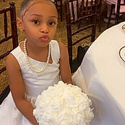 Myara joined the competition — help win amazing prizes! child, girl, white_dress, pearl_necklace, bouquet, white_roses, puckered_lips, formal_event, chair, table, carpet, hair_bun, earrings, indoor, person, flower_bouquet, decor, seated, smile, cute