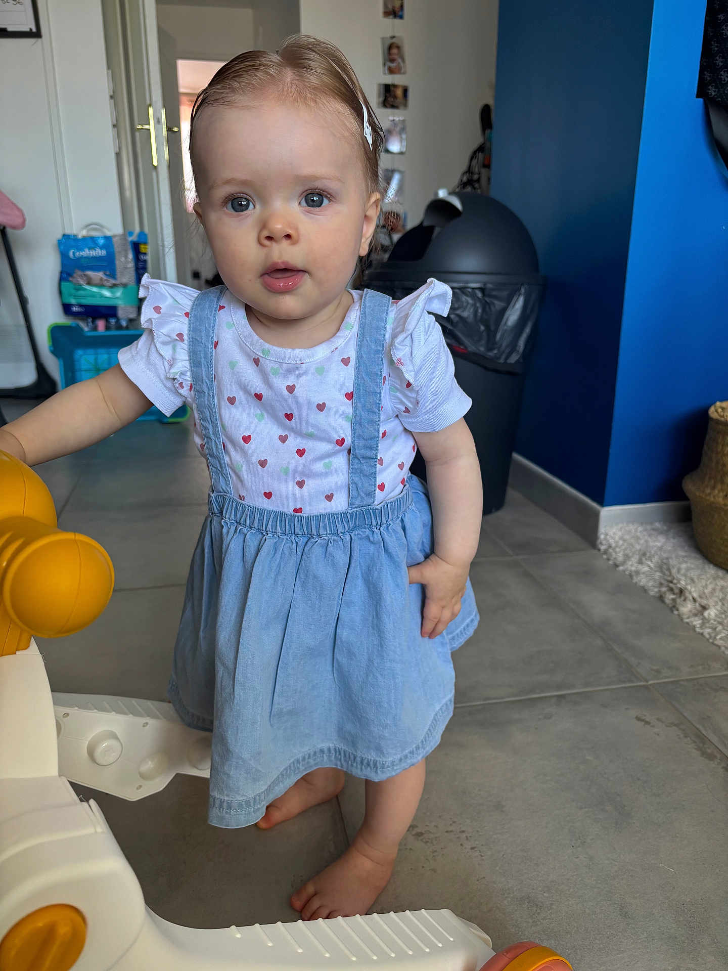 Arya participe au concours pour gagner de l'argent avec cette photo : toddler, child, indoor, dress, barefoot, toy, floor, face, blue_eyes, hair_clip, curious, standing, play, home, trash_bin, basket, tile_floor, young_child, person, casual