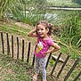 Santiago participe au concours pour gagner de l'argent avec cette photo : casual_clothing, child, curly_hair, daylight, fence, girl, grass, greenery, happy, nature, outdoor, pink_shirt, playful, polka_dot_pants, pond, sandals, smile, standing, trees, young