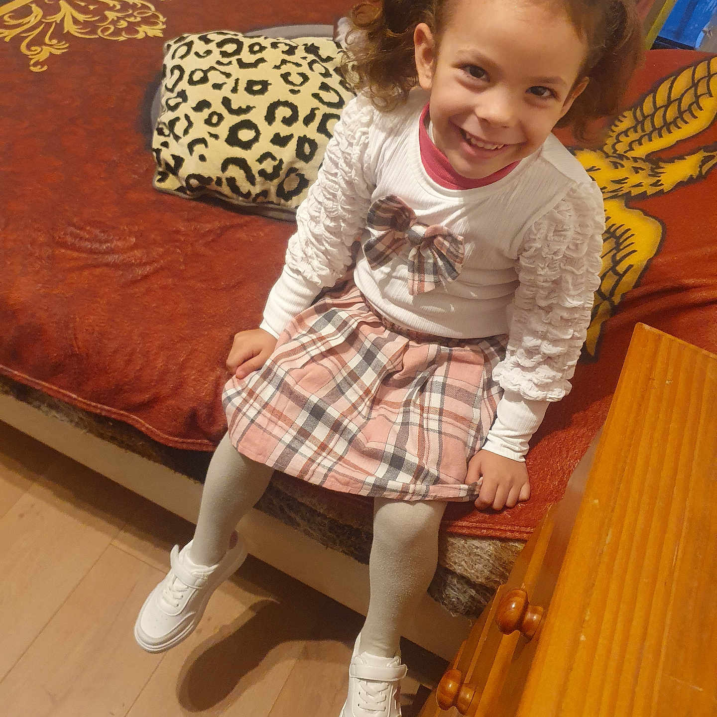 Matilde Filipa a rejoint le concours — aidez-le/la à gagner de superbes lots ! bed, blanket, child, cute, dresser, furniture, girl, happy, home, indoor, leopard_print, person, pigtails, pillow, plaid_skirt, sitting, smile, white_shoes, white_top, wooden_floor