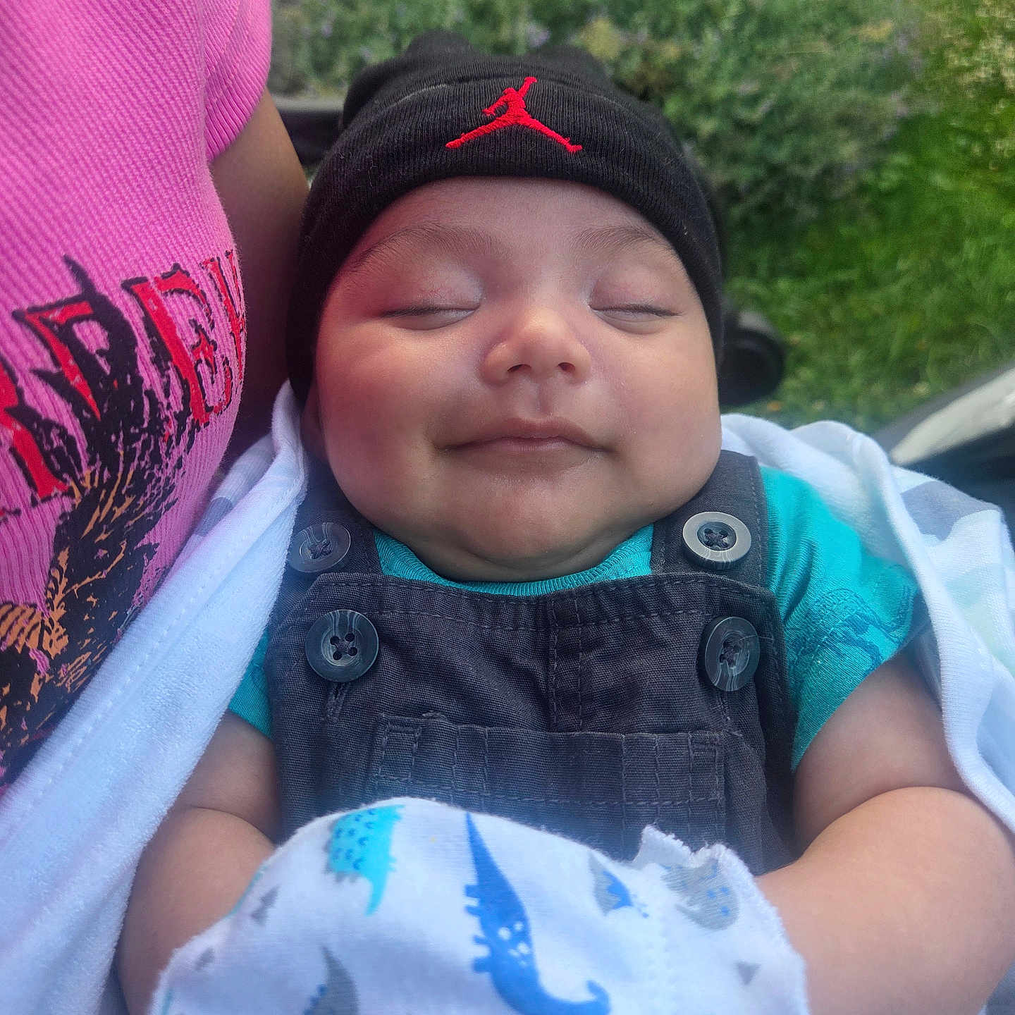 Heyden Carabantes joined the competition — help win amazing prizes! baby, beanie, black_hat, blanket, blue_shirt, child, closed_eyes, cozy, cute, dinosaur_pattern, greenery, happy, infant, outdoor, overalls, person, portrait, red_logo, smiling, soft_lighting