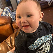 Landon is registered to the contest to win money with this photo: baby, black_shirt, blanket, child, close_up, couch, eyes, face, family_home, graphic_t_shirt, happy, indoors, infant, leather_furniture, living_room, pirate_design, portrait, sitting, smiling, wood_floor