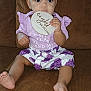 Star is registered to the contest to win money with this photo: baby, child, girl, infant, purple_clothing, headband, couch, brown_couch, wooden_sign, eight_months, sitting, indoors, cute, expression, holding, feet, face, person, portrait, clothing