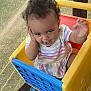 toddler, child, curly_hair, smiling, toy_cart, plastic_toy, outdoor, grass, playful, happy, striped_dress, person, waving, hand, face, seat, child_play, baby, cute, daylight