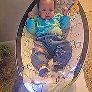 Nathan is registered to the contest to win money with this photo: baby, child, infant, swing, baby_swing, ripped_jeans, blue_shirt, toy, colorful_toy, carpet, indoor, comfort, clothing, footwear, baby_clothes, seat, face, person, relaxing, home