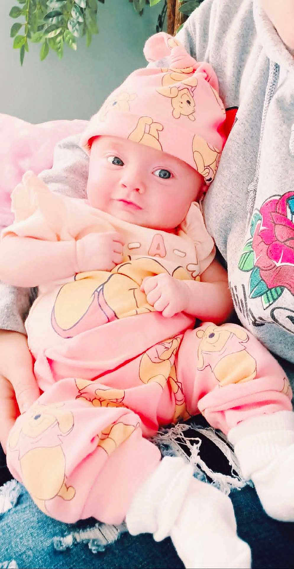 Destiny joined the competition — help win amazing prizes! baby, infant, pink_clothing, hat, winnie_the_pooh, person, hoodie, rose_design, indoor, green_leaves, cute, sitting, hands, face, eyes, cozy, soft_lighting, casual, denim, white_socks