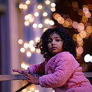 Athmiga joined the competition — help win amazing prizes! child, curly_hair, pink_jacket, wooden_railing, bokeh, lights, night, outdoor, portrait, cute, winter_clothing, warm, glowing, face, expression, young, person, curious, soft_texture, background