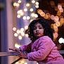 child, curly_hair, pink_jacket, wooden_railing, bokeh, lights, night, outdoor, portrait, cute, winter_clothing, warm, glowing, face, expression, young, person, curious, soft_texture, background